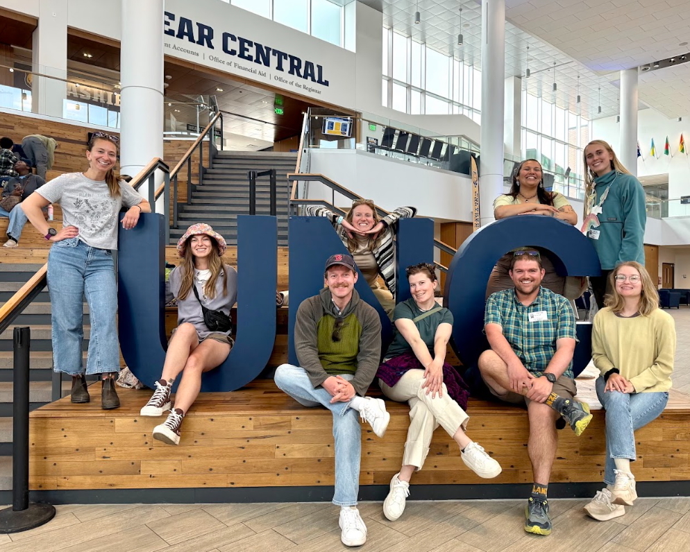 Youth Programs Educators & School Programs Manager sit in the UNC sign
